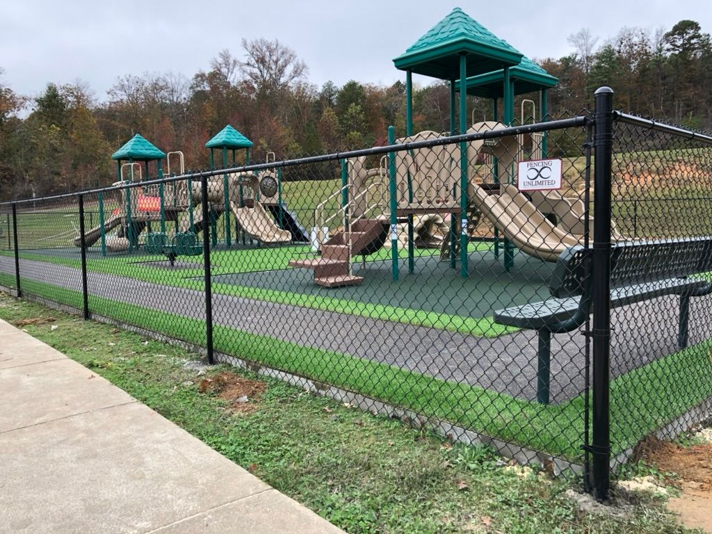 A chain link fence surrounds a playground in a park.