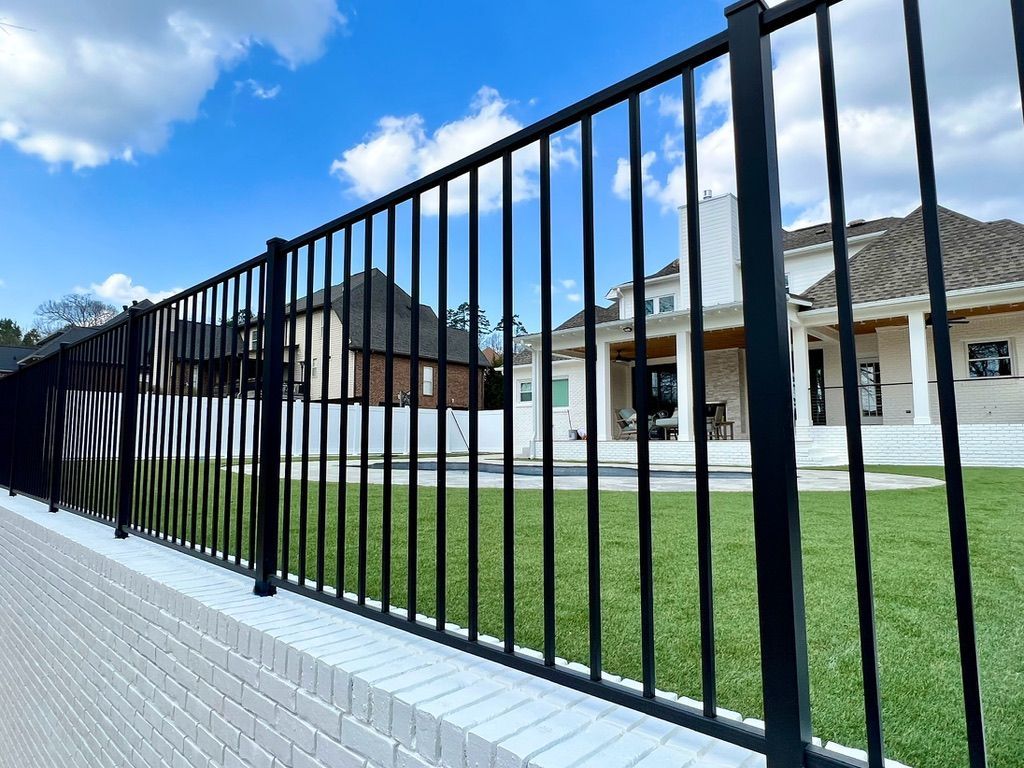 A black metal fence surrounds a large lawn in front of a house.