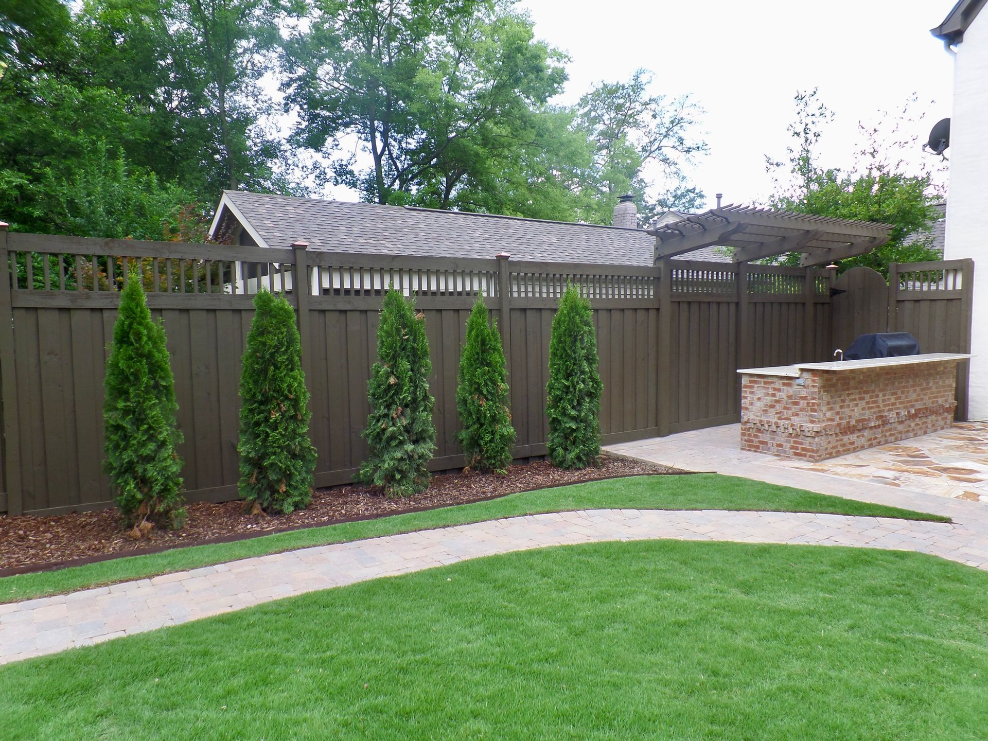 A wooden fence surrounds a lush green lawn in a backyard.
