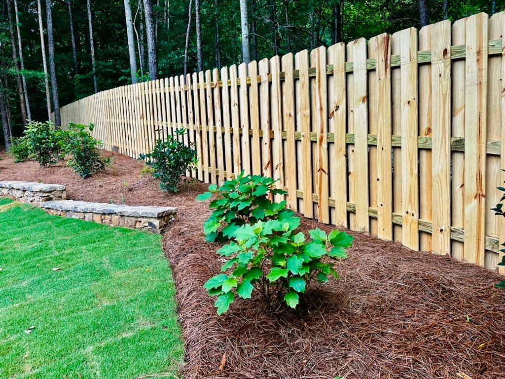 A wooden fence surrounds a lush green yard with trees in the background.