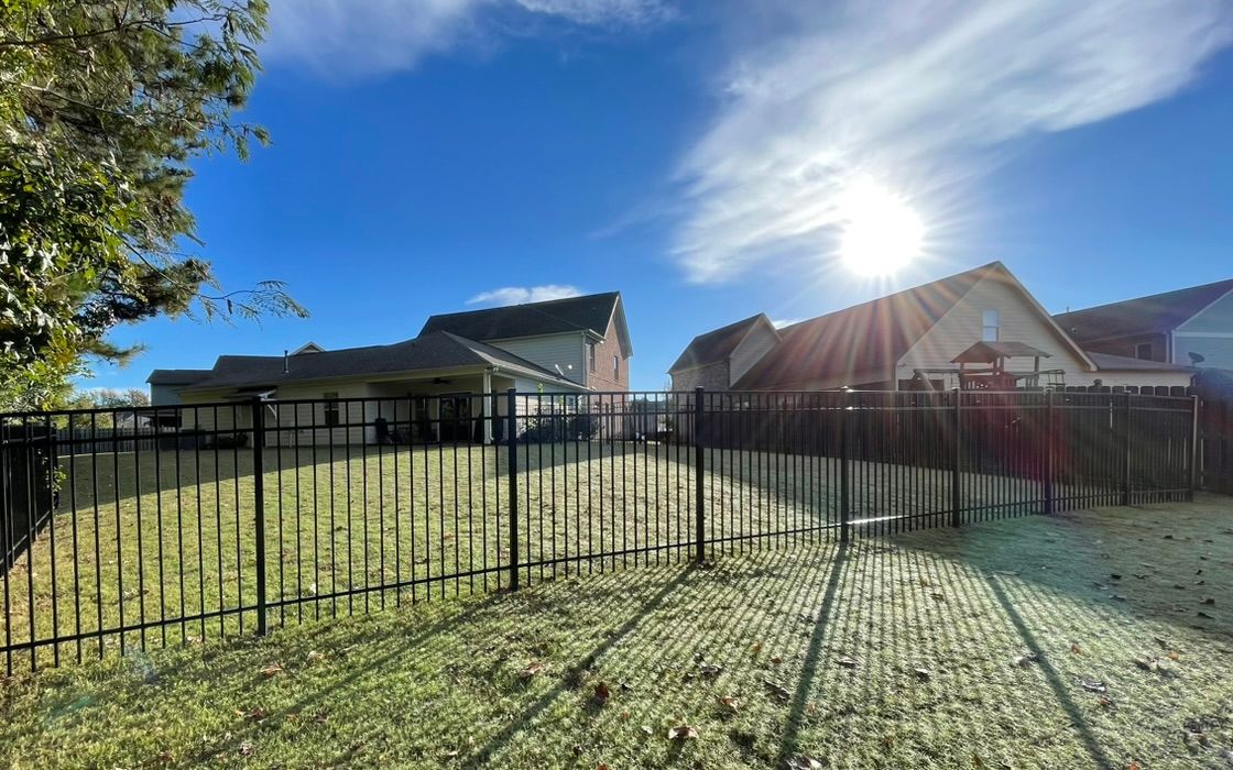 The sun is shining through the fence in the backyard of a house.