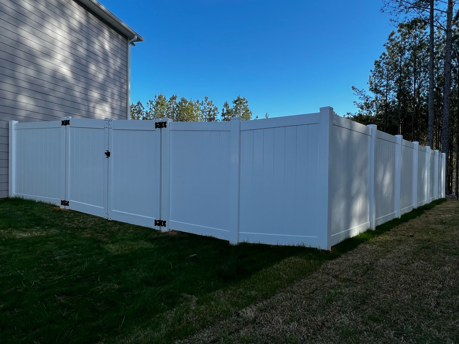 A white fence with a black gate is in the backyard of a house.