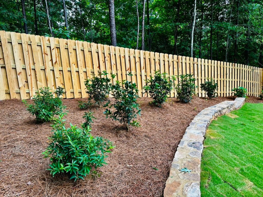 A wooden fence surrounds a lush green yard with trees in the background.