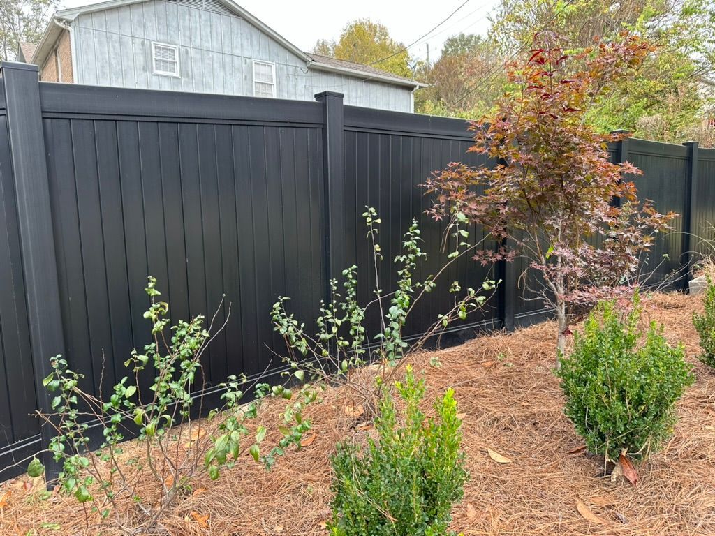 A black fence is surrounded by bushes and trees in a yard.