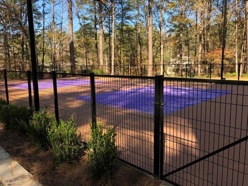 A fence surrounds a basketball court in the middle of a forest.