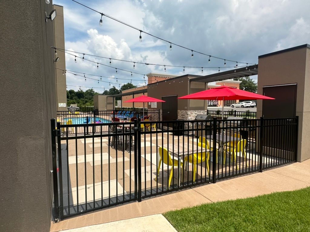 A fence surrounds a patio area with tables and chairs and red umbrellas.