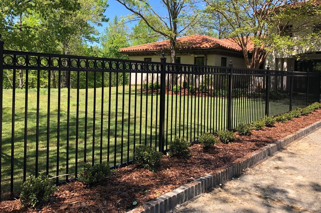 A black metal fence surrounds a large lawn in front of a house.