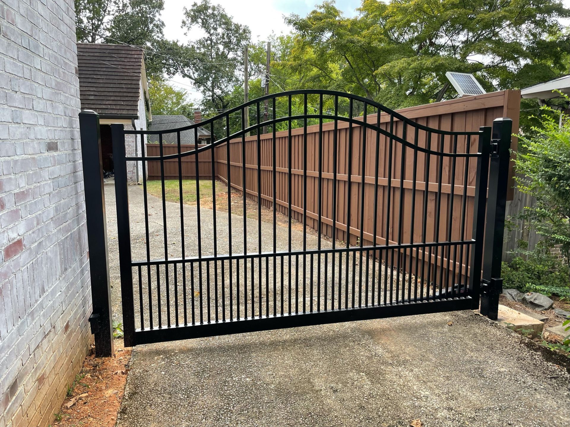 A black gate is open to a driveway next to a wooden fence.