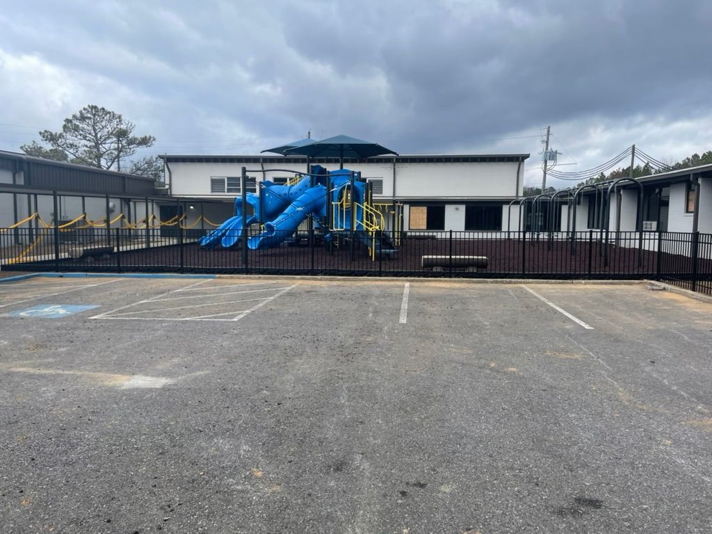 A playground is behind a fence in a parking lot.