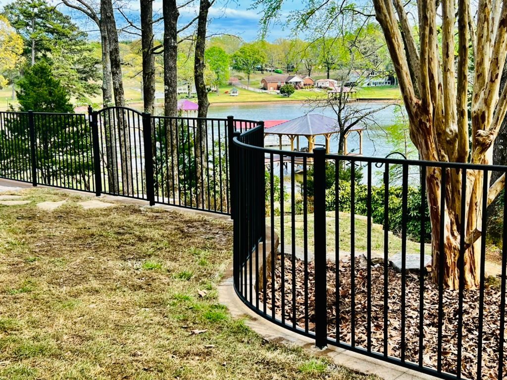 A black wrought iron fence surrounds a yard with a view of a lake.