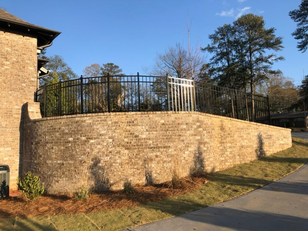 A large brick wall with a metal fence in front of a house.