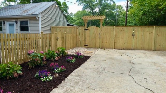 A wooden fence with a gate and flowers in front of a house.