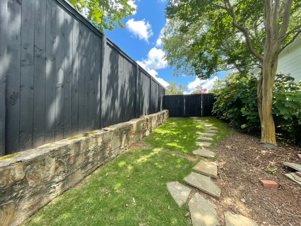 A black fence surrounds a lush green yard with a stone walkway leading to it.