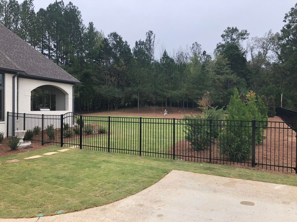 A black fence surrounds a lush green field in front of a house.