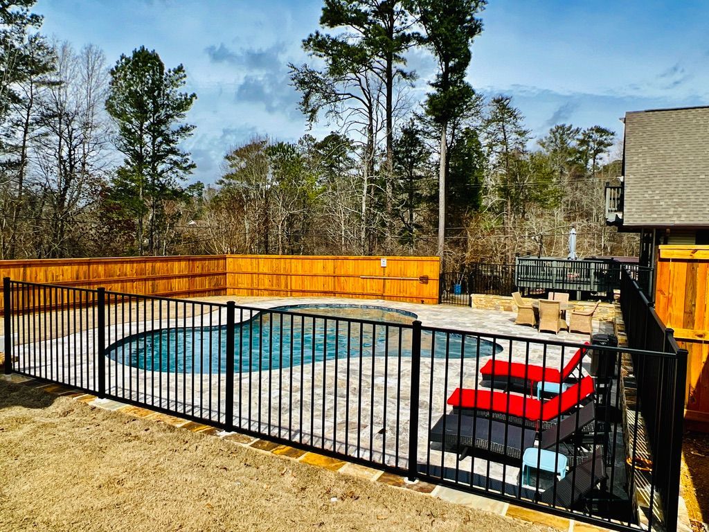 A fence surrounds a large swimming pool in a backyard.
