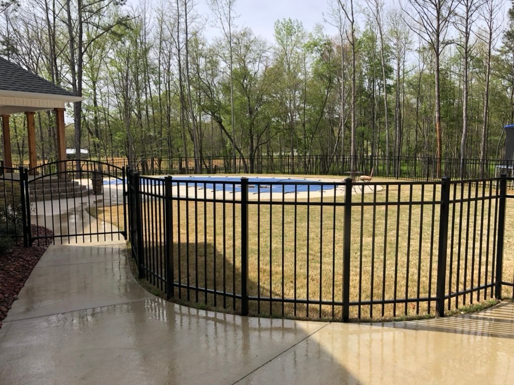 A black fence surrounds a swimming pool in a backyard.