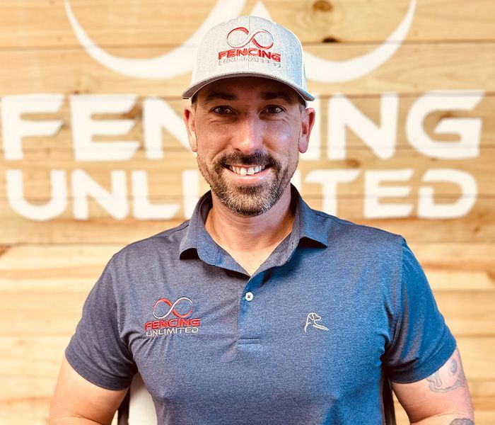 A man wearing a hat is standing in front of a sign that says fencing unlimited