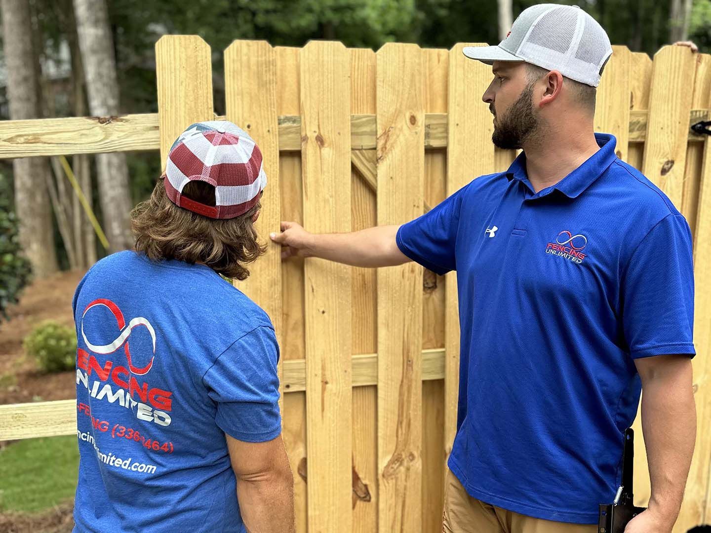 Two men are standing next to a wooden fence.