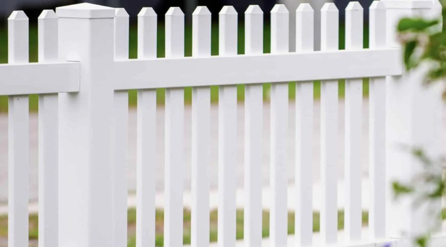 A clean white vinyl picket fence with pointed tops and a sturdy square post cap.