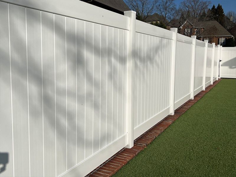 A white fence is surrounding a lush green yard.