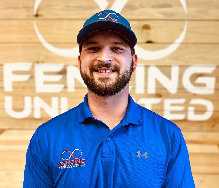 A man wearing a blue shirt and hat is smiling in front of a sign that says fencing united