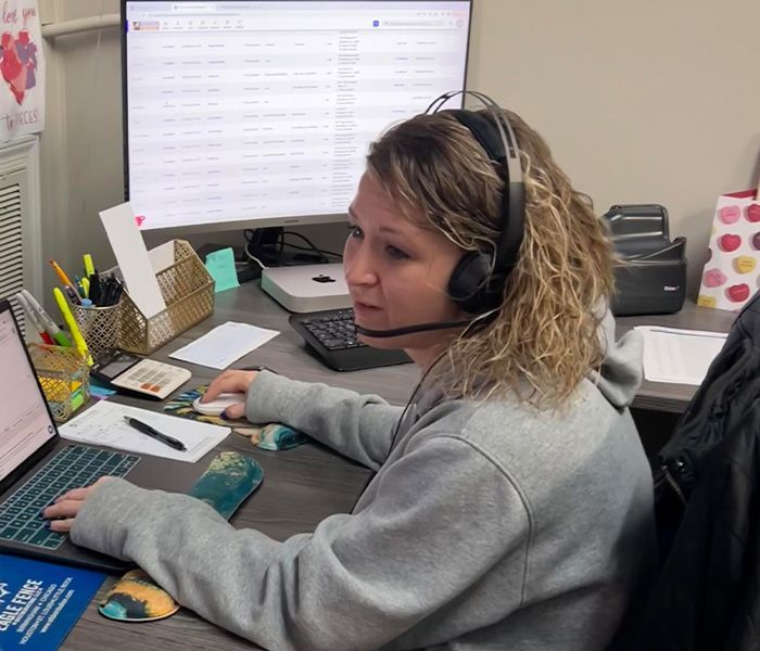 A woman wearing headphones is sitting at a desk using a laptop computer.