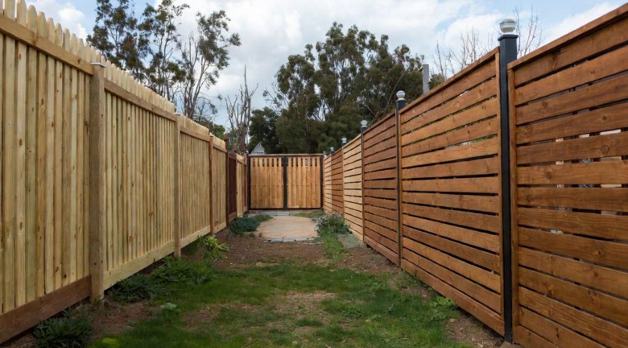 A path leads between two different styles of wooden fences, with a closed wooden gate at the end.