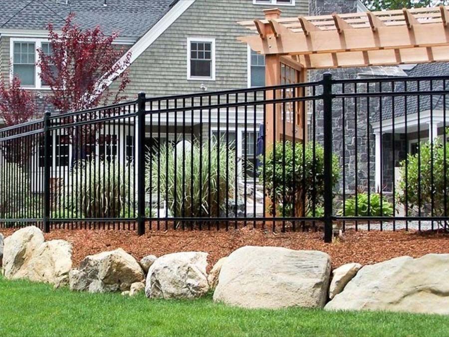 A metal fence surrounds a rocky area in front of a house