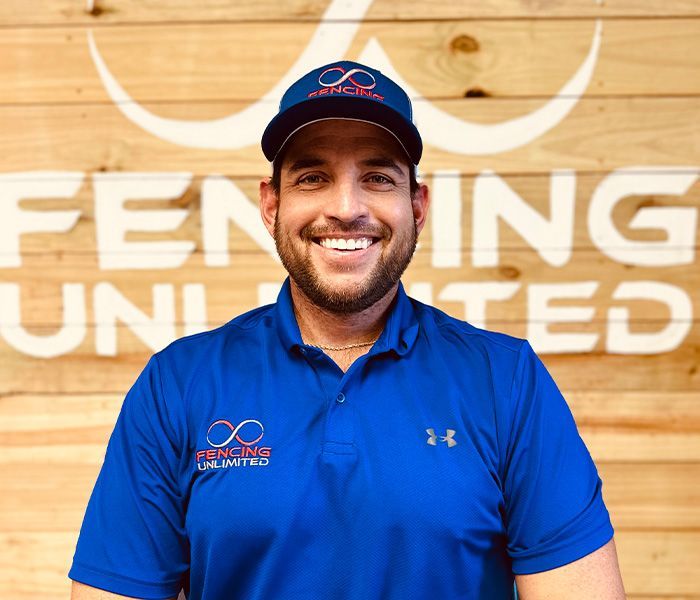 A man is smiling in front of a sign that says fencing unlimited