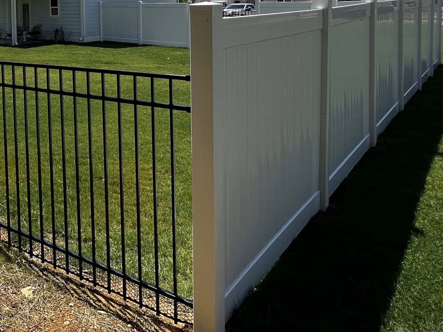 A white fence with a black metal fence in front of a house.