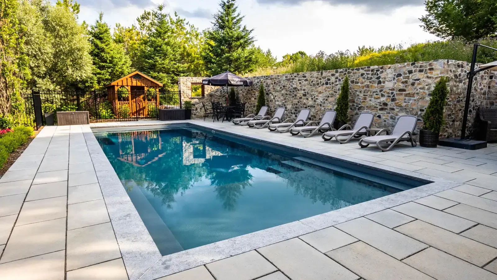 A large swimming pool surrounded by chairs and a stone wall.