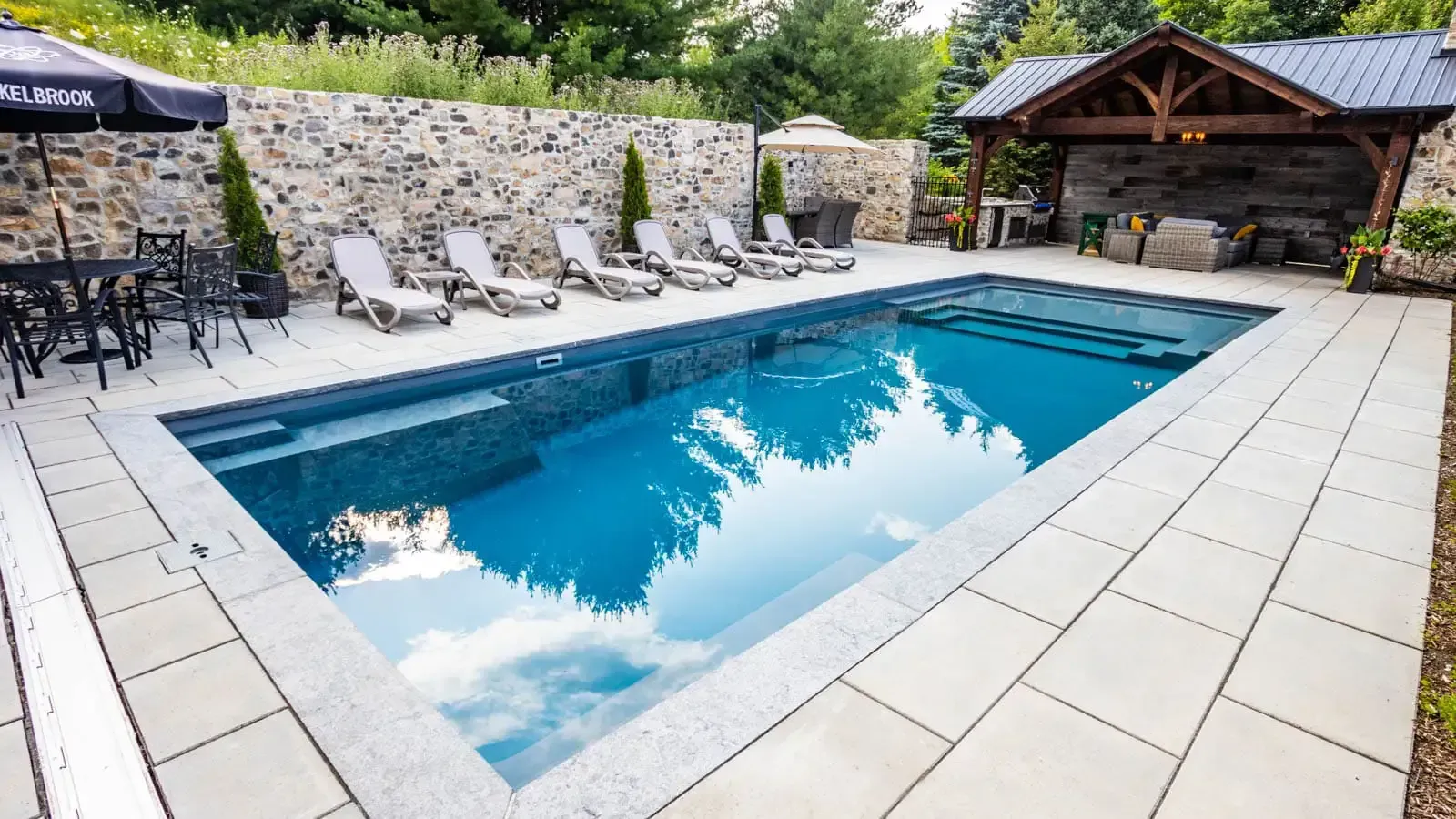A large swimming pool surrounded by chairs and tables in a backyard.