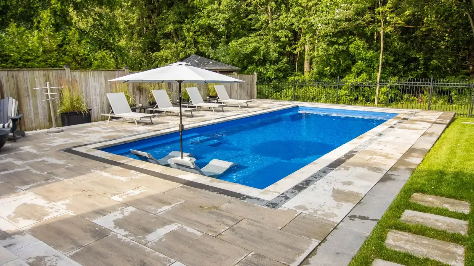 A large swimming pool surrounded by chairs and umbrellas in a backyard.