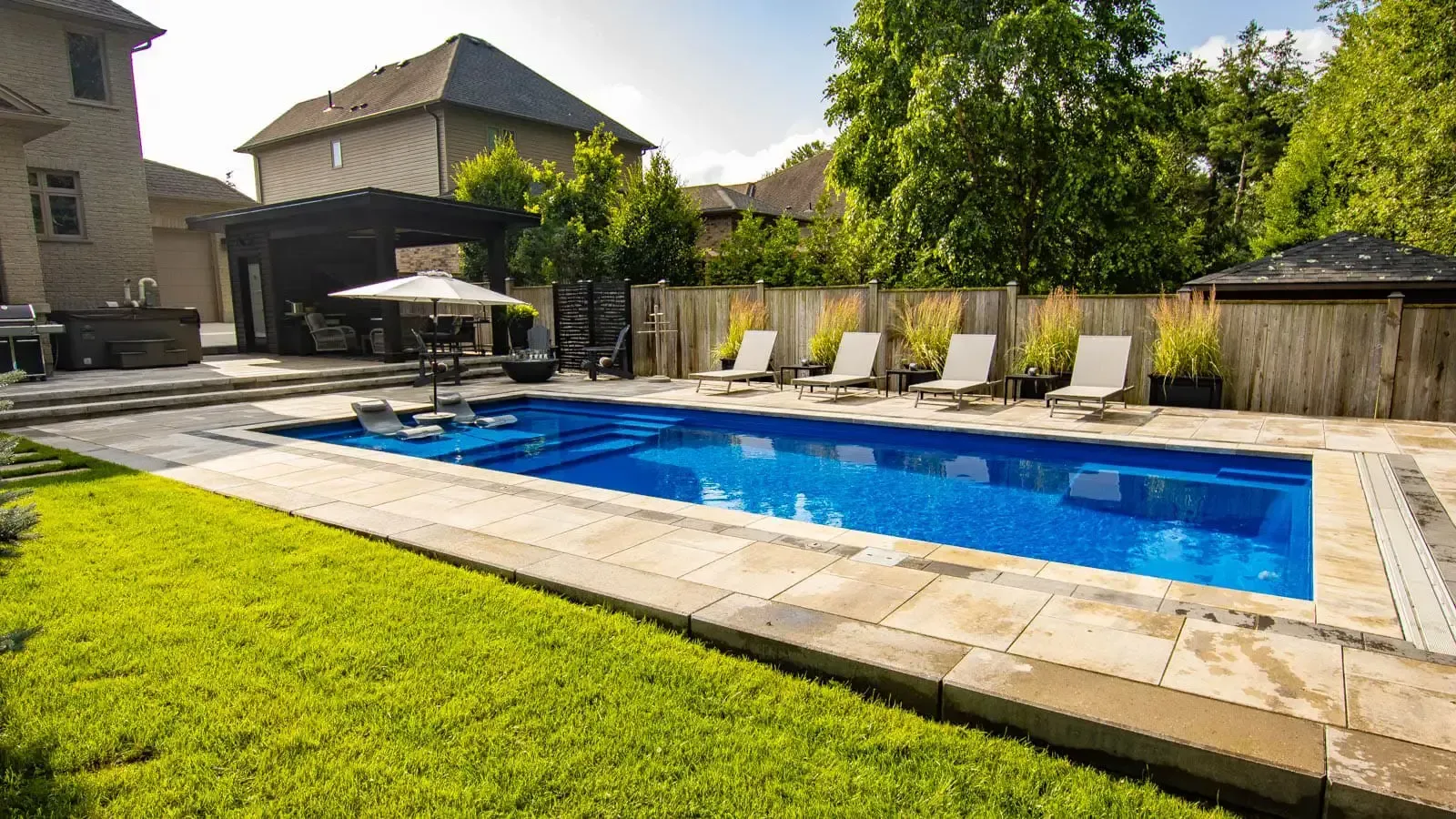 A large swimming pool surrounded by chairs and umbrellas in a backyard.