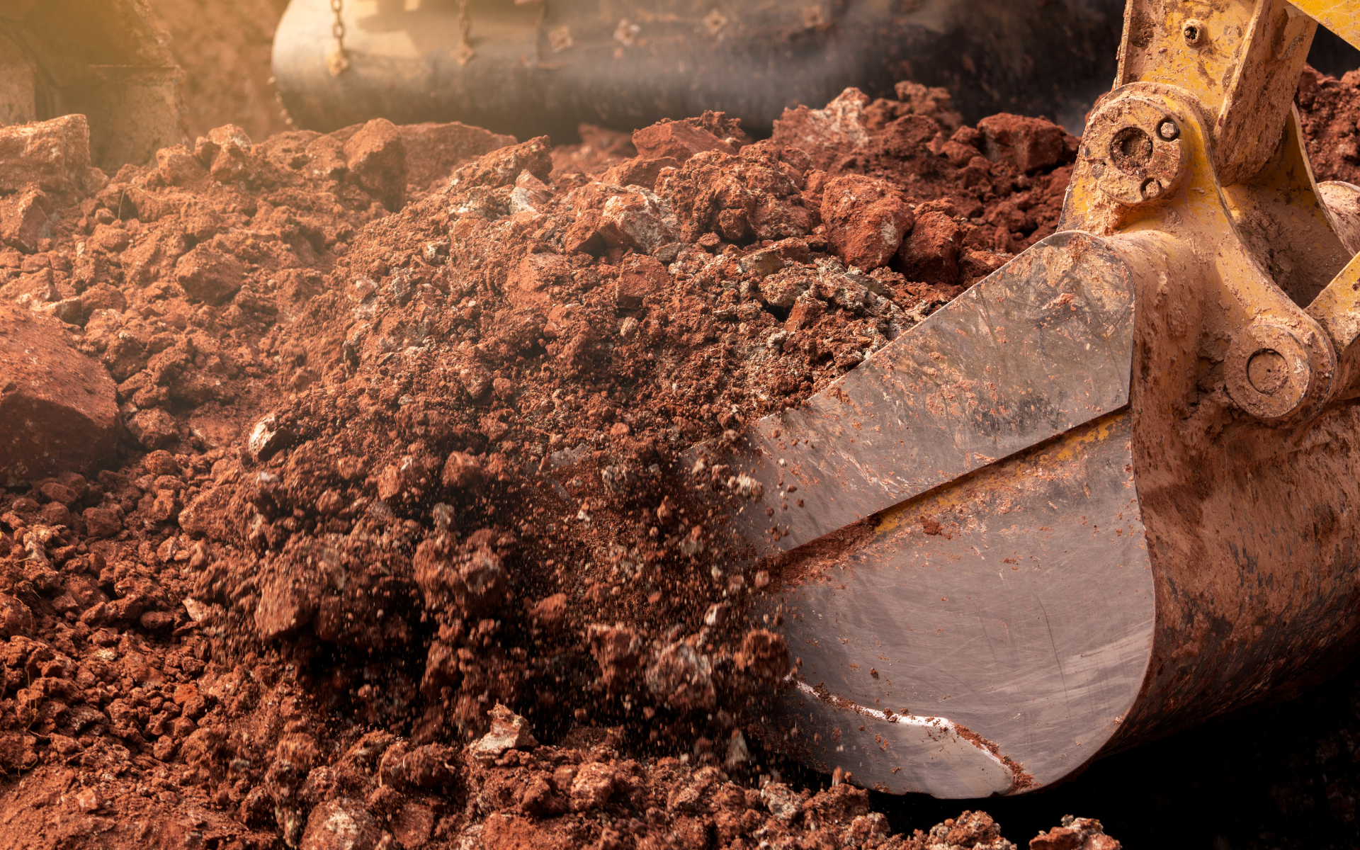 Large excavator scoop digging into soil to grade a property and fix drainage issues