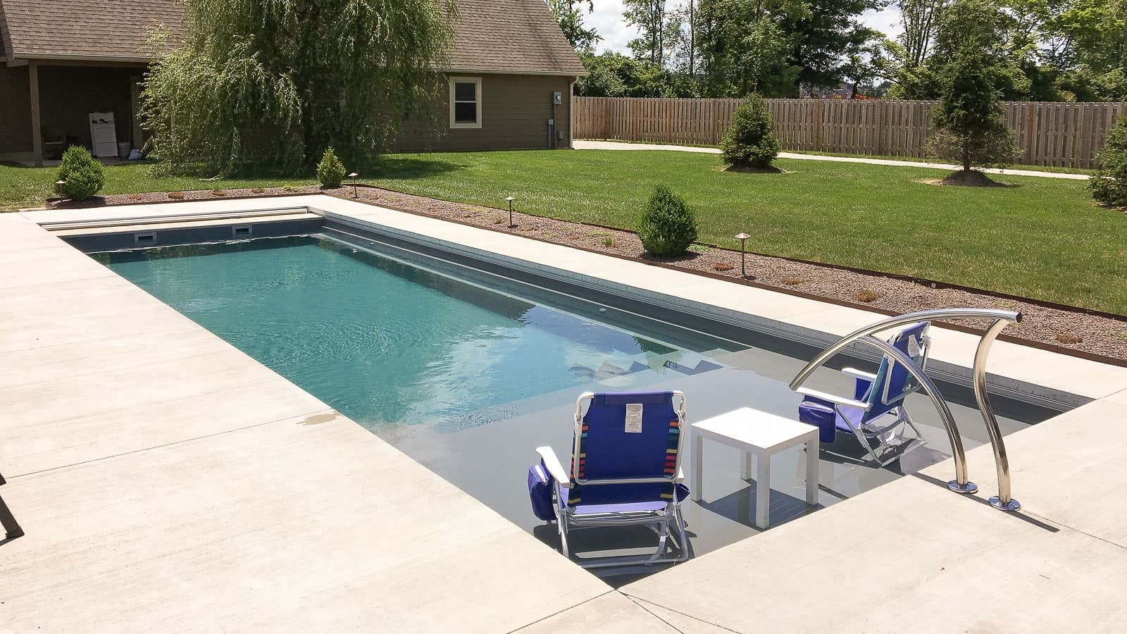 A large swimming pool with chairs and a table in front of it