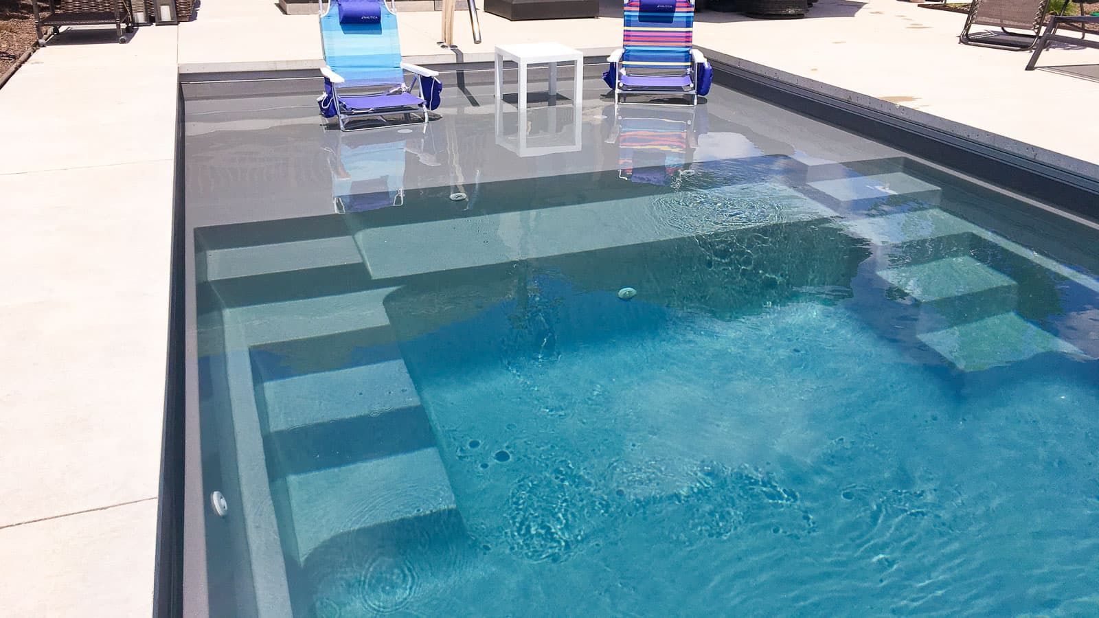 A large swimming pool with chairs and a table in the background.