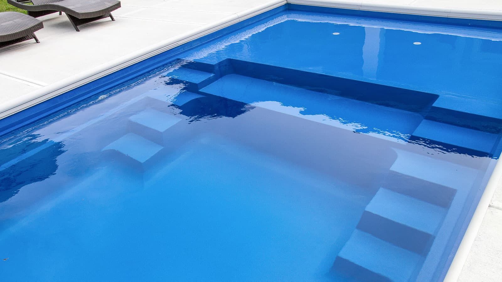 A large blue swimming pool with stairs and chairs in the background.