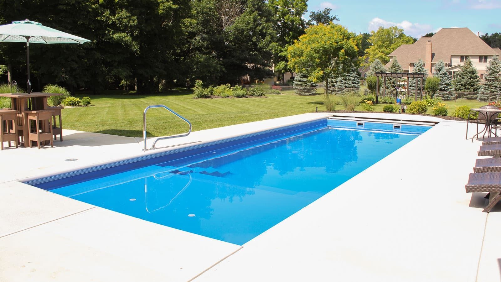 A large swimming pool in a backyard with tables and chairs around it.
