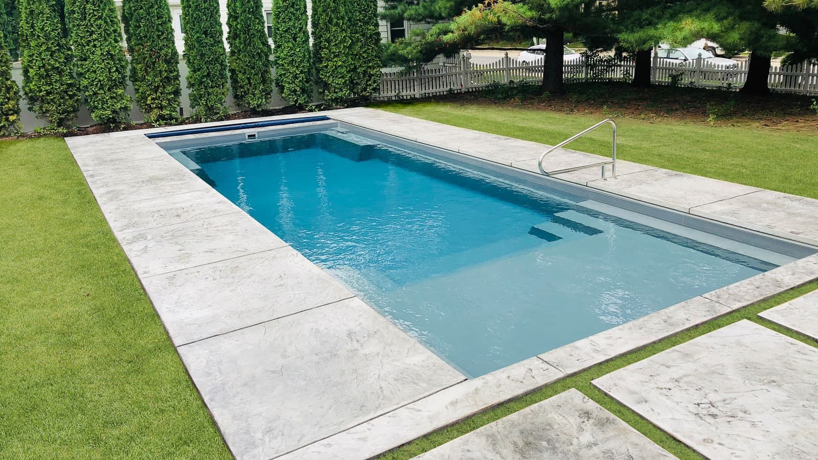 A large swimming pool is surrounded by grass and trees in a backyard.