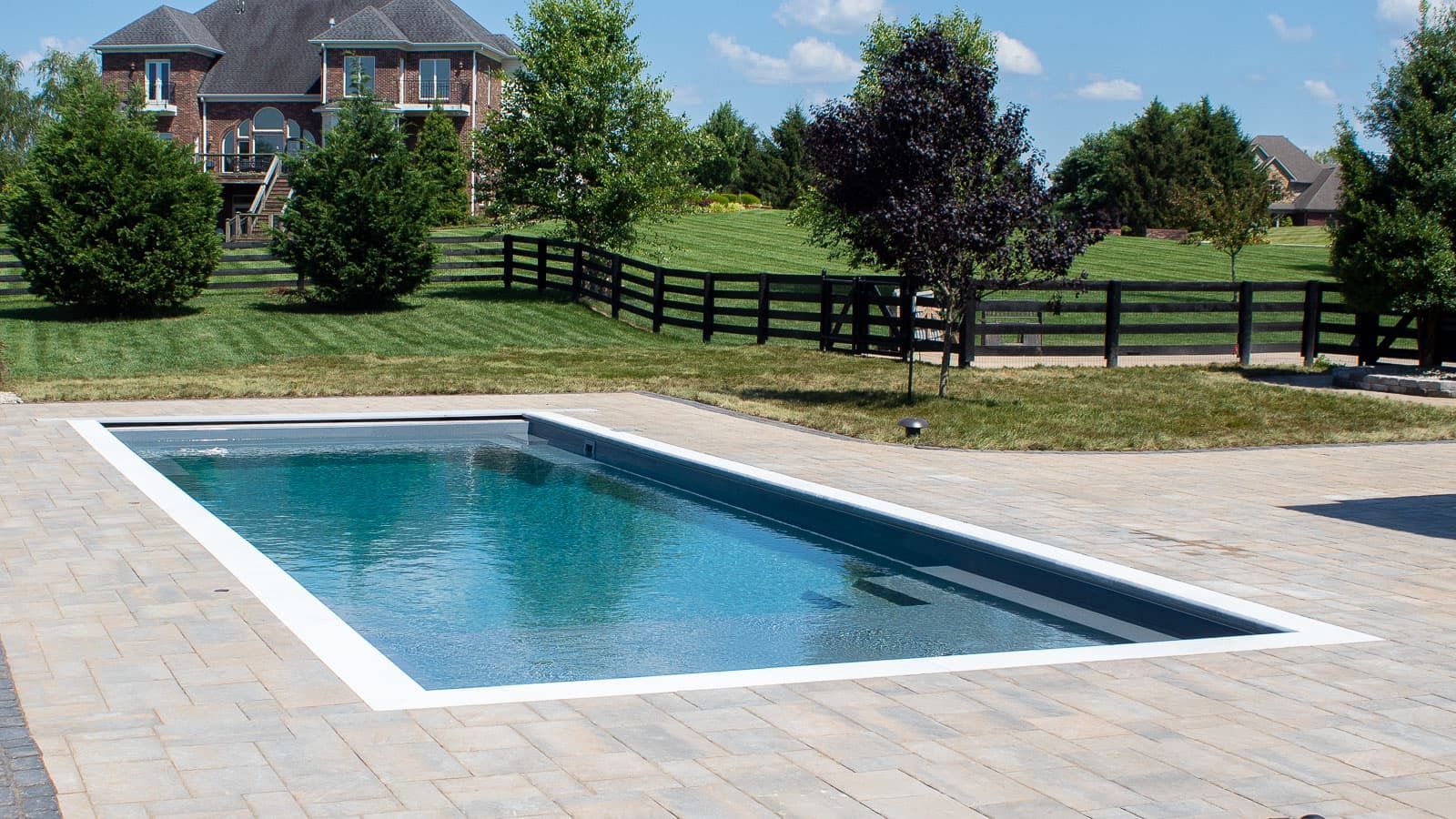 A large swimming pool in a backyard with a house in the background