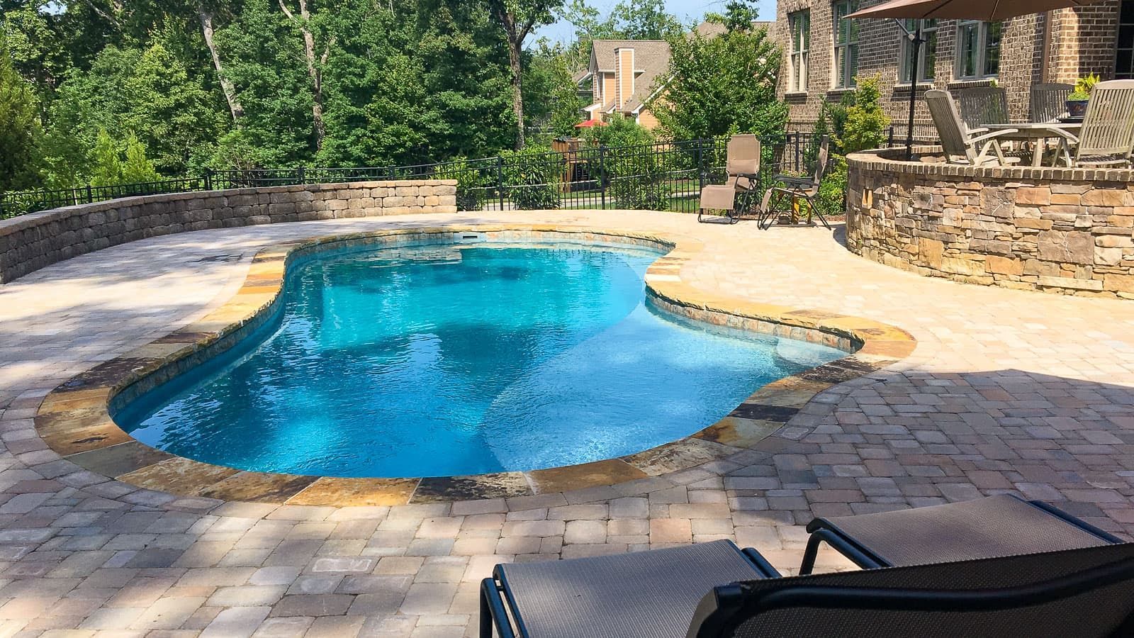 A large swimming pool is surrounded by a patio with chairs and umbrellas.