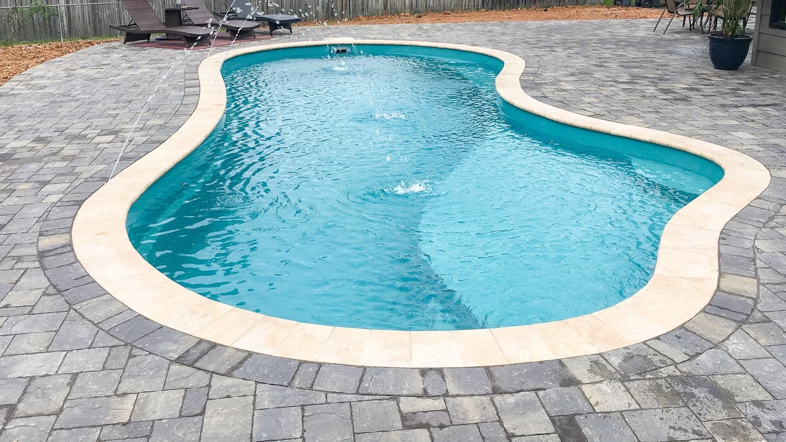 A large swimming pool is sitting on top of a brick patio.