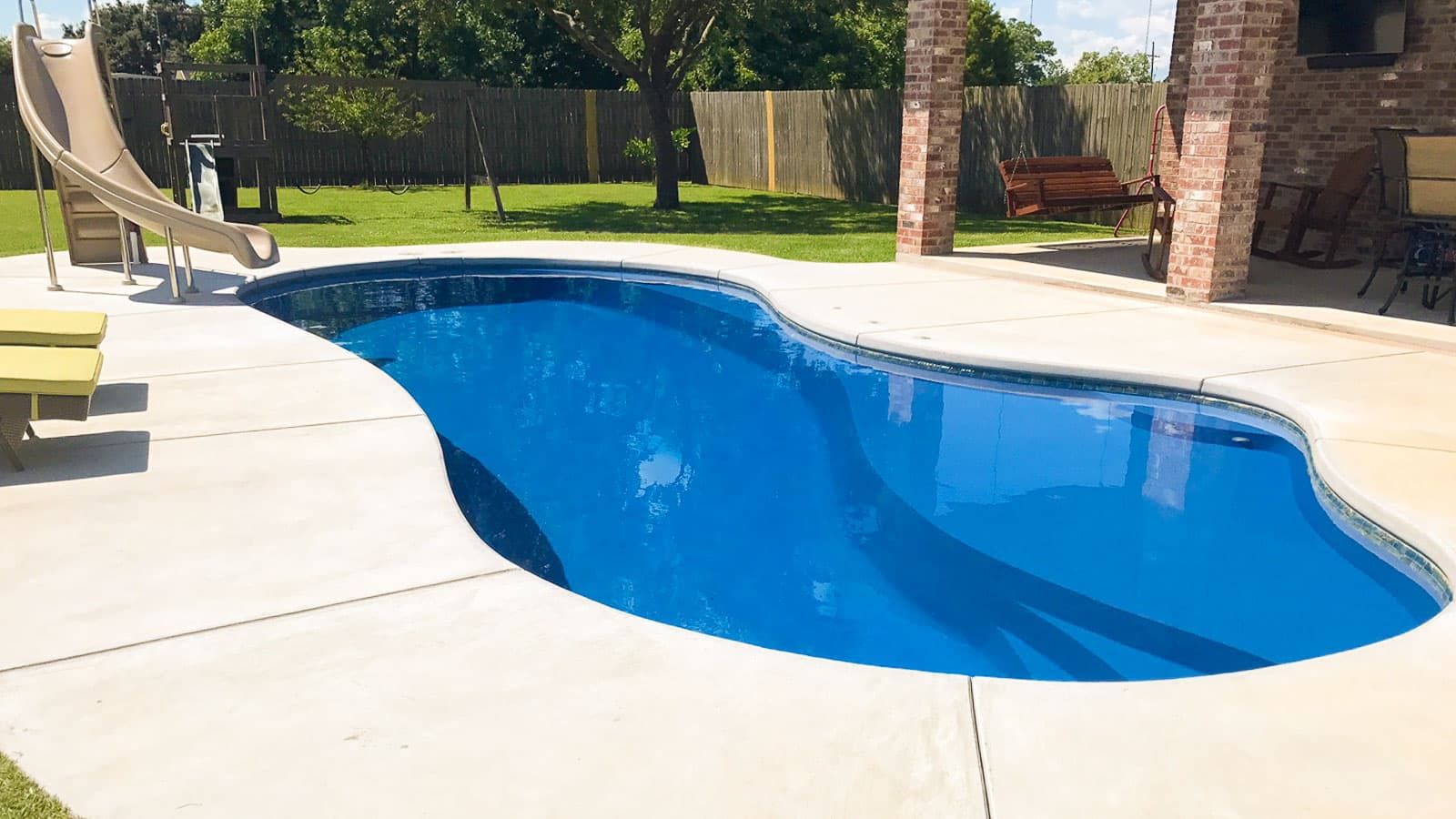A large blue swimming pool with a slide in the backyard.
