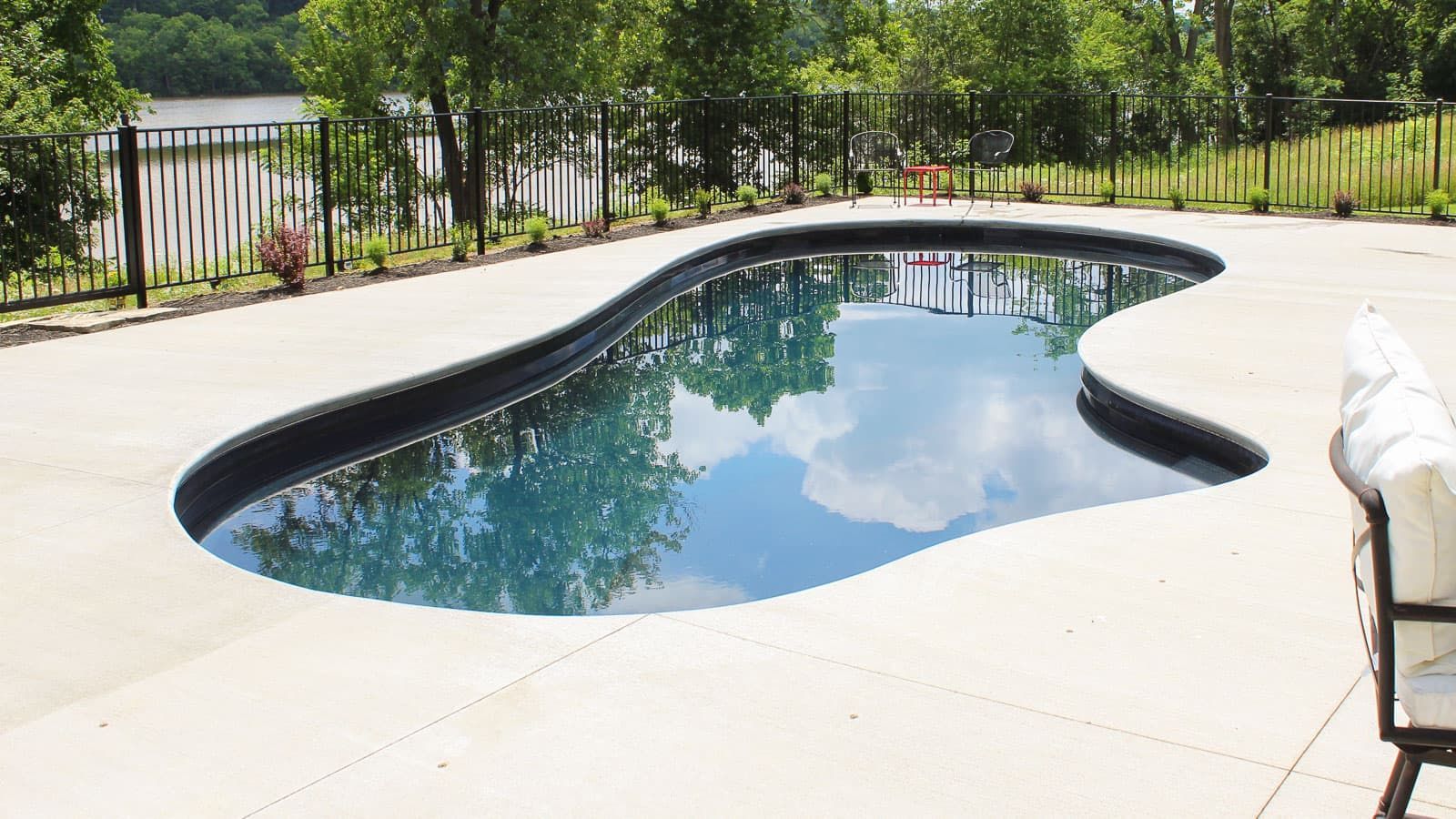 The Inspiration swimming pool, volcanic black, is surrounded by a fence and trees.