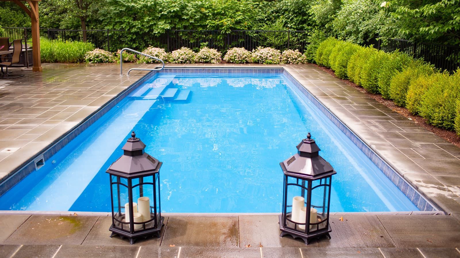 Two lanterns are sitting next to a large swimming pool.