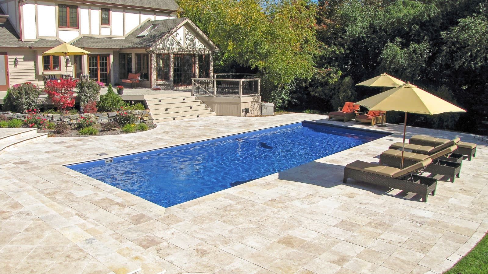 A large swimming pool surrounded by chairs and umbrellas in front of a house