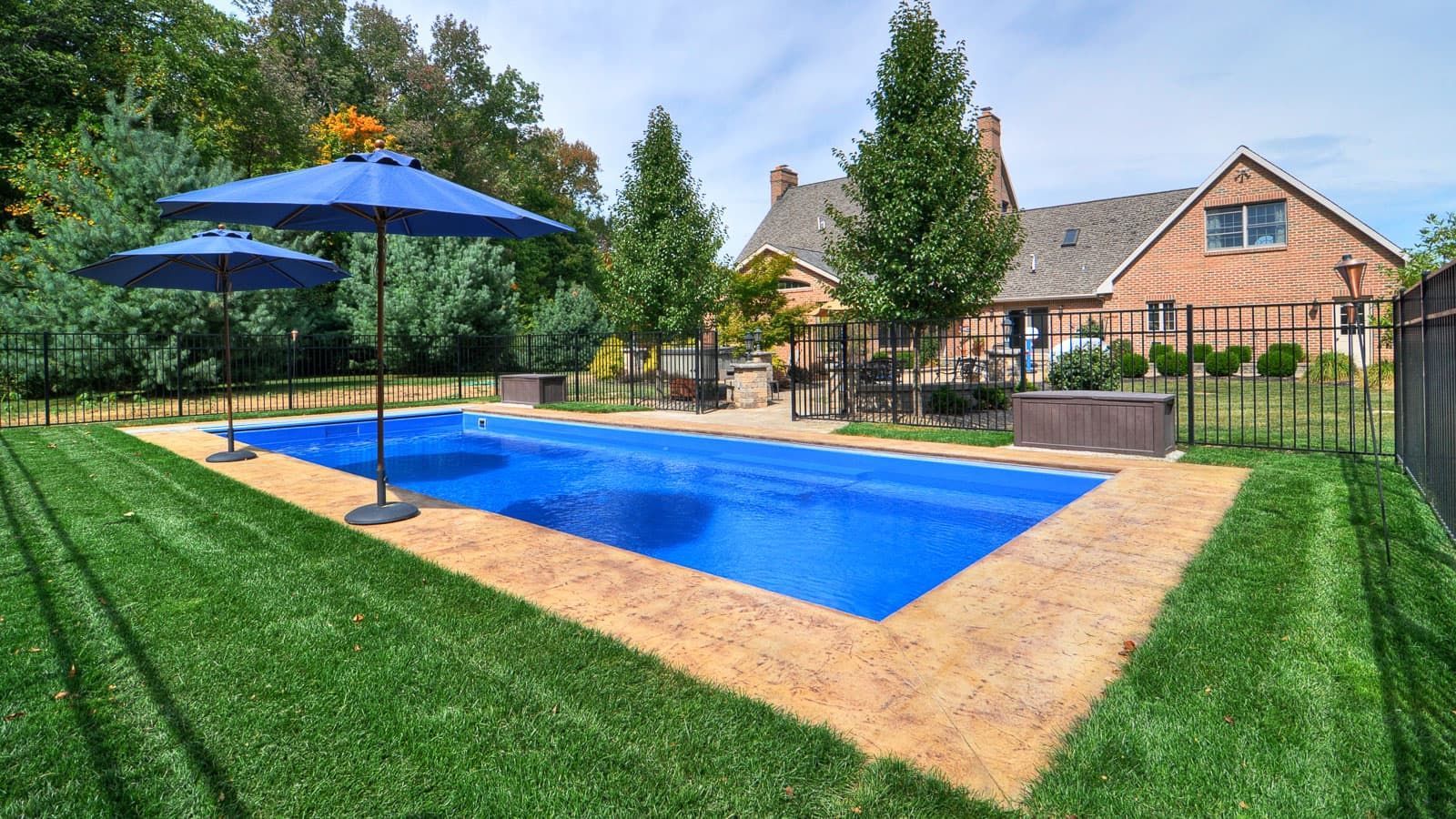 A large swimming pool with two blue umbrellas in front of a brick house.