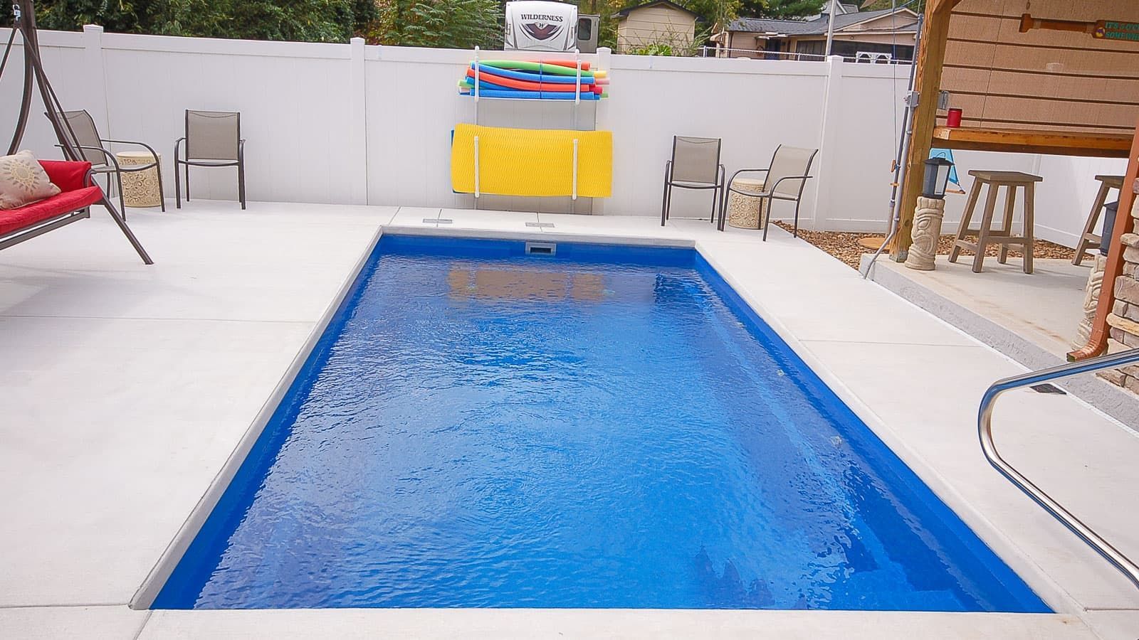 A small swimming pool in a backyard with chairs and a swing.