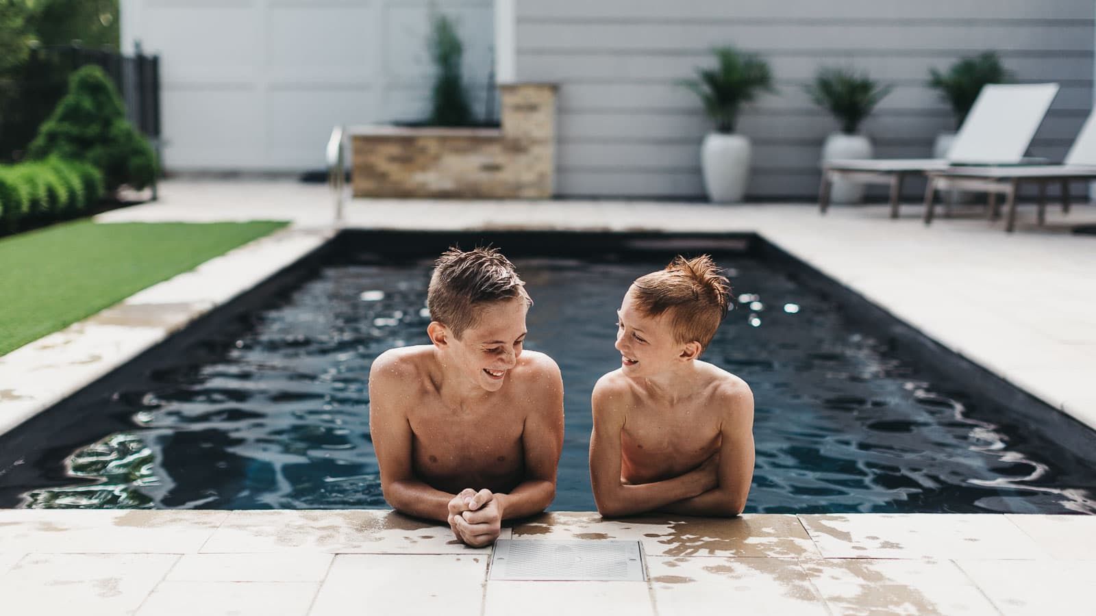 Two young boys are sitting on the edge of a swimming pool.